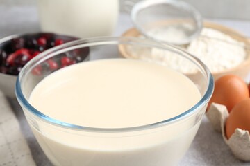 Liquid dough in bowl, berries and ingredients on light grey table, closeup