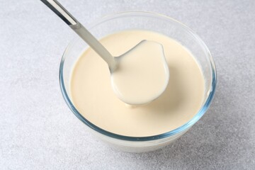 Taking liquid dough from bowl with ladle on light grey table, closeup
