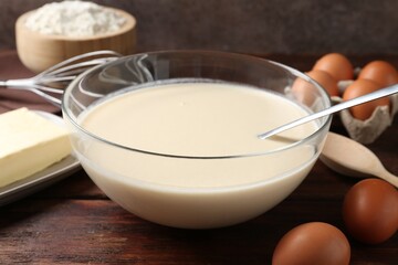Liquid dough in bowl and ingredients on wooden table, closeup