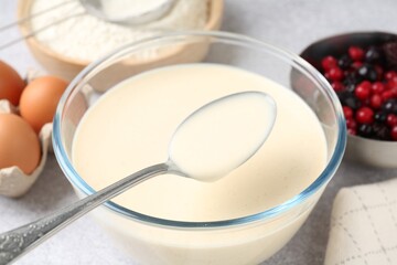 Taking liquid dough from bowl with spoon on light grey table, closeup
