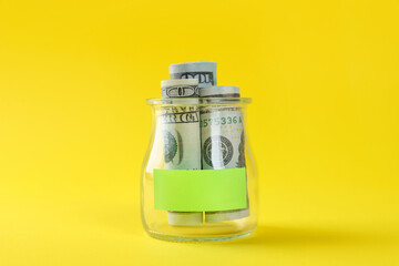 Jar with blank note and money on yellow background