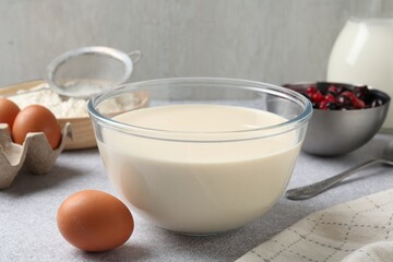 Liquid dough in bowl, berries and ingredients on light grey table, closeup