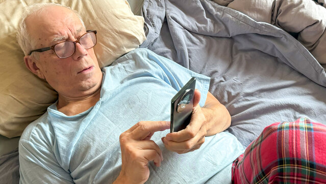 Senior Man Using Smartphone In Bed For Concepts Of Digital Inclusion, Active Aging, Remote Communication, Elderly Tech Use, And Everyday Life Visuals For Healthcare And Lifestyle Content - Powered by Adobe