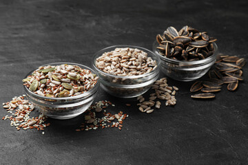 Different seeds in bowls on black textured table, closeup