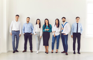 Obraz premium Full length portrait of confident business people in formal clothes looking at camera and smiling indoors. Company employees or group of staff standing in office. Business people portrait.