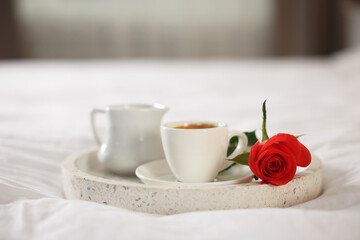Tray with coffee, cream and rose on bed in hotel room, closeup