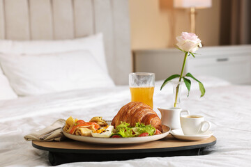 Tray with delicious breakfast and rose on bed in hotel room, closeup. Space for text