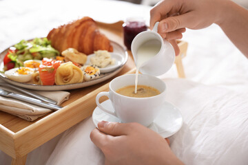 Man pouring cream into coffee while having breakfast in bed, closeup. Hotel room service