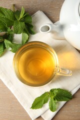 Cup of delicious tea and mint on wooden table, flat lay