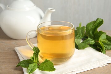 Cup of delicious tea and mint on wooden table, closeup