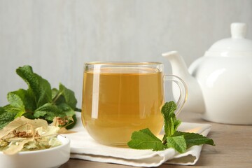 Cup of delicious tea, linden leaves and mint on wooden table, closeup