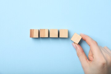 Woman with wooden cubes on light blue background, top view