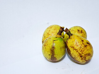 matoa fruits (Pometia pinnata) are displayed on a white surface, one partially peeled to reveal the...