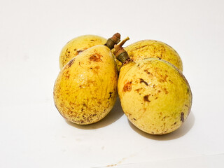 matoa fruits (Pometia pinnata) are displayed on a white surface, one partially peeled to reveal the...