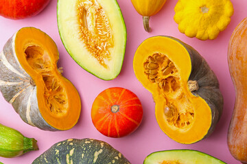 Many fresh pumpkins and other gourds on pink background, flat lay
