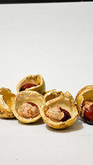 Exotic peeled matoa fruit (Pometia pinnata) showing its glossy brown seed and pale, cracked aril against the broken yellow-green husk on a white background.