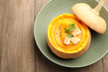 Tasty pumpkin cream soup with parsley and croutons served in pumpkin on wooden table, closeup. Space for text