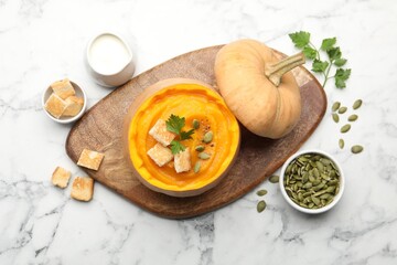 Tasty pumpkin cream soup with seeds, parsley and croutons served in pumpkin on white marble table, flat lay
