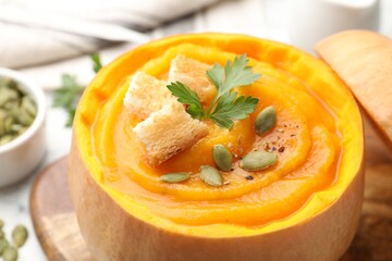 Tasty pumpkin cream soup with seeds, parsley and croutons served in pumpkin on white table, closeup