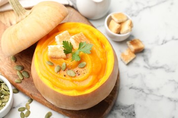 Tasty pumpkin cream soup with seeds, parsley and croutons served in pumpkin on white marble table, closeup
