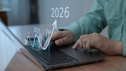 Close-up of hands working on laptop with futuristic financial graphs and projections for 2026, symbolizing growth and analytics.
