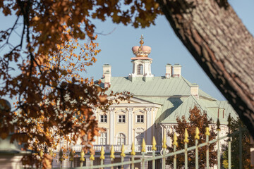 Close view of Grand Menshikov Palace in Oranienbaum framed by autumn leaves and decorative fence under clear blue sky.