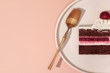 Bento cake with layers of chocolate and cherry, topped with whipped cream and a cherry, served on a white plate with a golden spoon, creating a delightful dessert experience