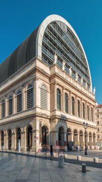 Hyperlapse of Lyon's opera house featuring neoclassical architecture combined with a modern glass dome roof. A historical and touristic landmark with statues under blue sky. Side view timelapse