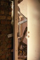 Partially open door reveals debris, collapsed beams, and crumbling walls inside an abandoned building illuminated by warm afternoon sunlight.