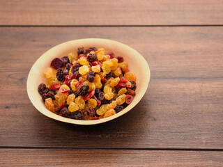 A bowl of dried fruit with yellow and red raisins, cranberries. The bowl is on a wooden table. Natural high sugar and glucose content. Popular snack.
