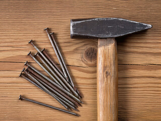 An old hammer and rusty nails resting on a wooden surface. Suitable for repair, construction, and craft-themed projects.
