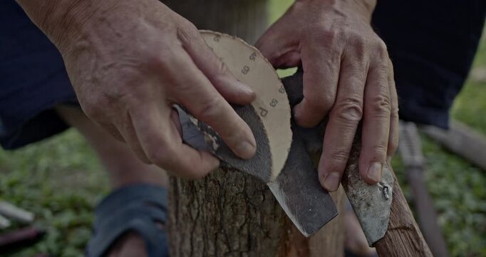 Witness the meticulous process of an axe being sharpened by hand using sandpaper. This close-up shot captures the detailed work and features authentic sounds of metal on abrasive.