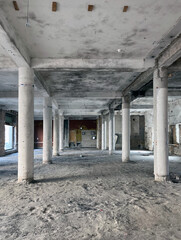 Empty, abandoned industrial interior with concrete columns, exposed beams, and worn floors, showing signs of decay and unfinished renovation.