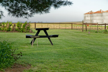 Empty picnic table on green lawn near farm silos