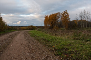 Golden hour light illuminates the clouds above a winding country road in the autumn twilight. Farm buildings and forest line the horizon in this atmospheric Estonian landscape.