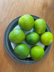 A plate of limes on a wooden table.