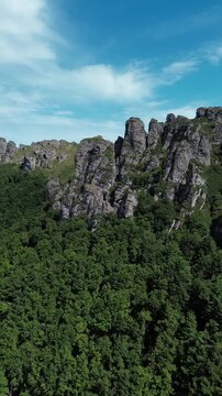 Rocky peaks of Babin Zub mountain in Stara Planina National Park, Serbia, rise above green forests under a blue sky. Aerial view from drone. Vertical 4k footage