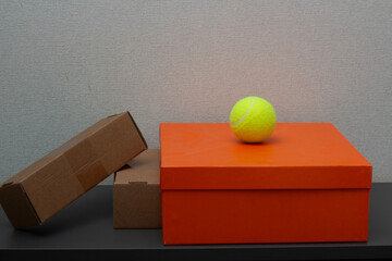 Horizontal photo. Yellow tennis ball sits on orange cardboard box on gray cabinet shelf. Concept of sport, Black Friday sale, shoe, discount, 11 november, online shopping, cyber monday. Copy space