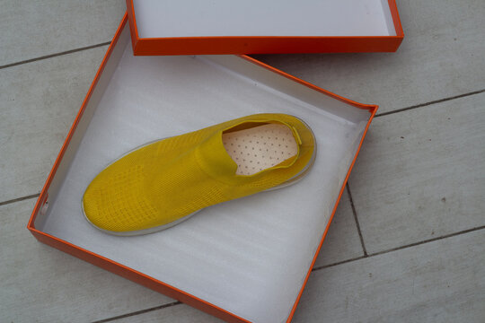 Horizontal photo. Top view. Yellow sport sneakers inside orange box on gray floor. Concept of discount, Black Friday, purchase, shoe sale, 11 november, cyber monday, online shopping, football, run