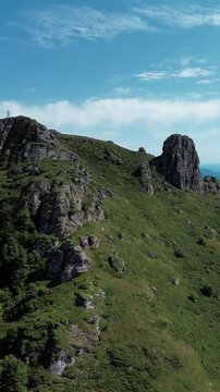 Rocky peaks of Babin Zub mountain in Stara Planina National Park, Serbia, rise above green forests under a blue sky. Aerial view from drone. Vertical 4k footage