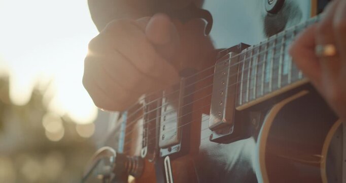 Close-up of hand strumming electric guitar in summer sunlight
