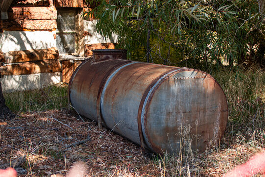 An old galvanized metal tank used for water storage near an abandoned cabin in the woods.