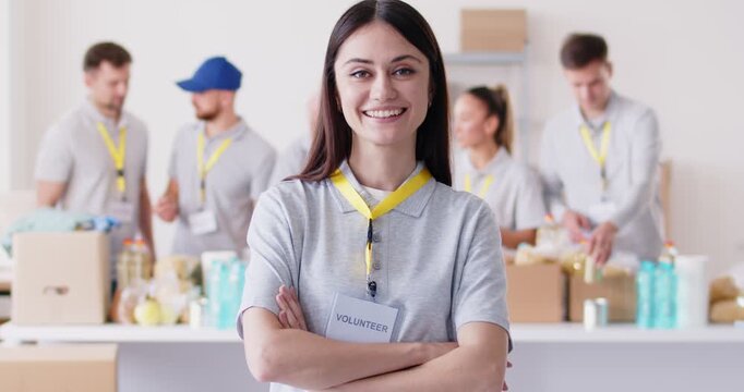 Young female volunteer girl supervisor smiling looking at camera, working in charitable food foundation to make donation charity, stuff, basic need provisions, free meal for people in need, food bank