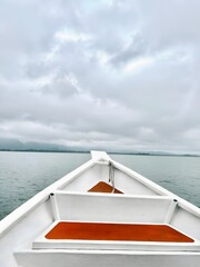 View from a white boat's bow on calm waters under a cloudy sky, showcasing a serene journey towards the horizon, highlighting nature's vastness and peaceful travel