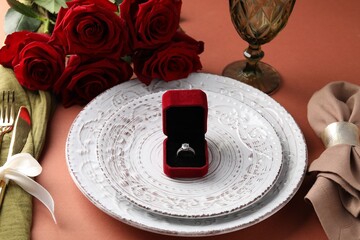 Beautiful table setting for romantic dinner, box with engagement ring and roses on color background, closeup