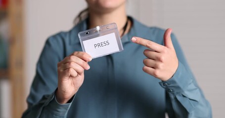 Journalist showing her badge indoors, closeup. Camera moving up
