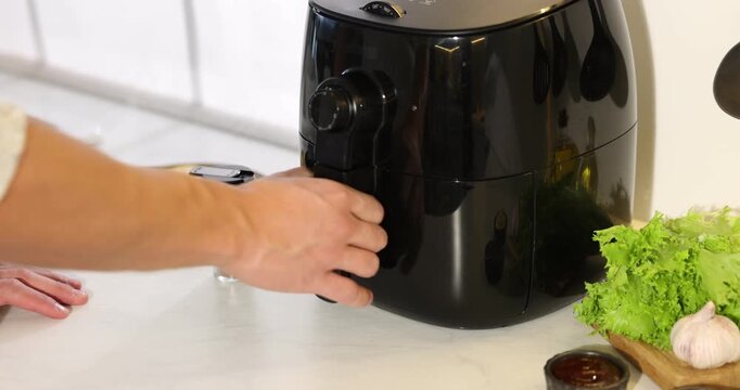 Man adding spices to french fries in air fryer at white marble countertop, closeup. Camera moving in