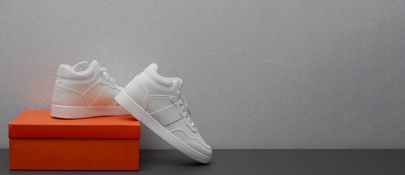 Horizontal banner with copy space for text. White sport sneakers near an orange box on gray shelf. Concept of purchase, shoe sale, discount, Black Friday, 11 november, online shopping, cyber monday