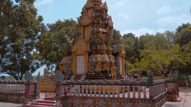 Massive golden stupa with statues of Yakshas demon guardians on its levels stand in the temple grounds of Wat Svay Romeat Pagoda in Siem Reap, Cambodia. Shot in motion