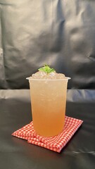 Cold Beverage with Ice in Clear Plastic Cup on Red Checkered Cloth in Dark Background